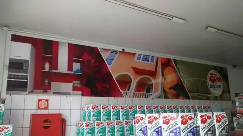 Painel impresso vermelho com casas e frutas sobre parede, acima de pilhas de produtos de tinta