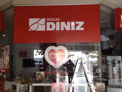 Vitrine de ótica com painel vermelho e logo branco Óticas Diniz e adesivo de coração