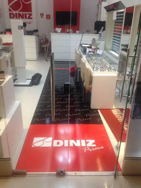 Adesivo de piso vermelho e preto com logo Diniz Prime na entrada de uma ótica