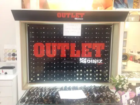 Vitrine interna de ótica com painel preto perfurado e OUTLET em vermelho Diniz