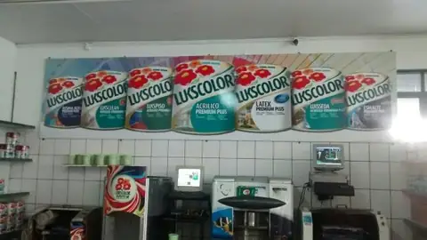 Painel com latas de tinta Luxcolor sobre balcão de loja de tintas